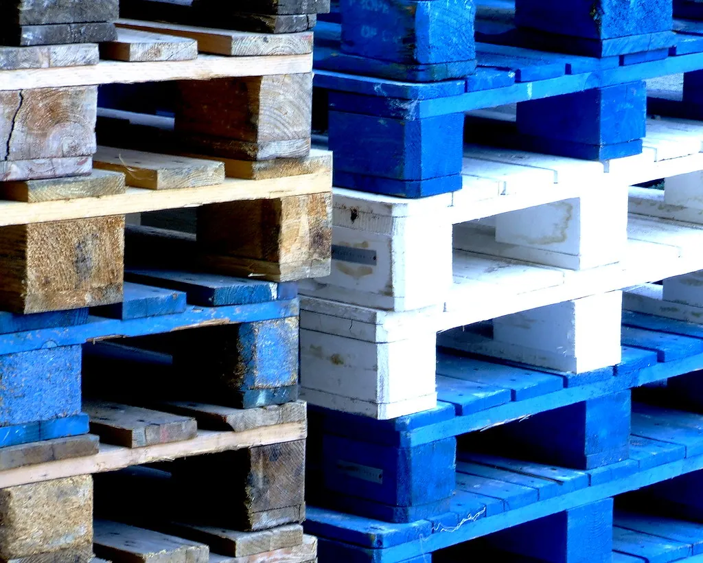 Tarimas de plástico azules y blancas estibadas junto a tarimas de madera
