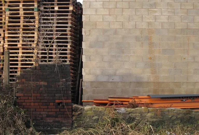 Pilas de tarimas de madera estibadas junto a un muro de block
