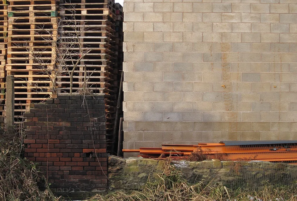 Pilas de tarimas de madera estibadas junto a un muro de block