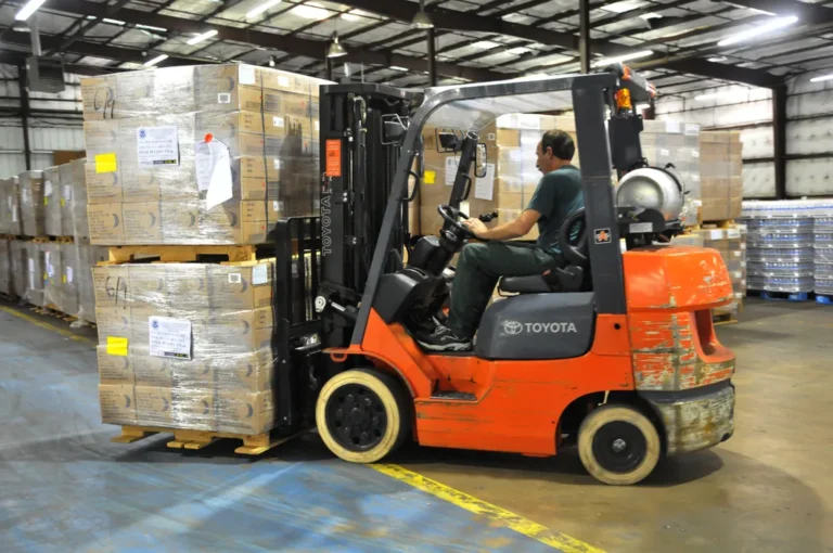 Montacargas de gas LP moviendo tarimas de madera con cajas dentro de un almacén