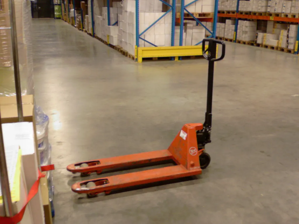 Patín hidráulico manual naranja en el pasillo de un almacén con racks de tarimas